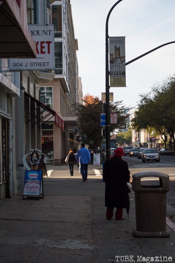 A sharply-dressed man stands in front of a convenience store on J Street. Photo M.Hershenow. 2014.
